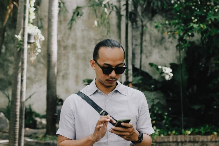 man in white button up shirt wearing black sunglasses holding black smartphone